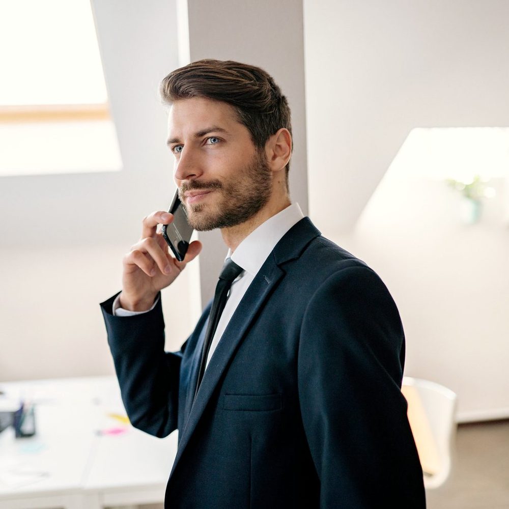 Un professionista in abito blu al telefono con un cliente, in un ufficio luminoso